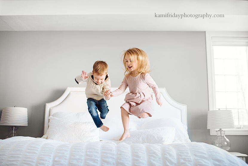 NH lifestyle family photographers captures Bedford NH brother and sister jumping on their parent's bed.