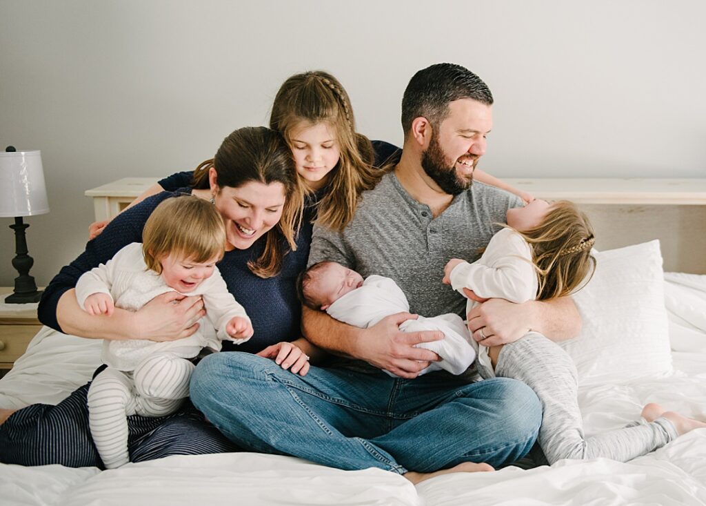 Family playing on bed with newborn baby and siblings during a lifestyle newborn photography session in Nashua NH