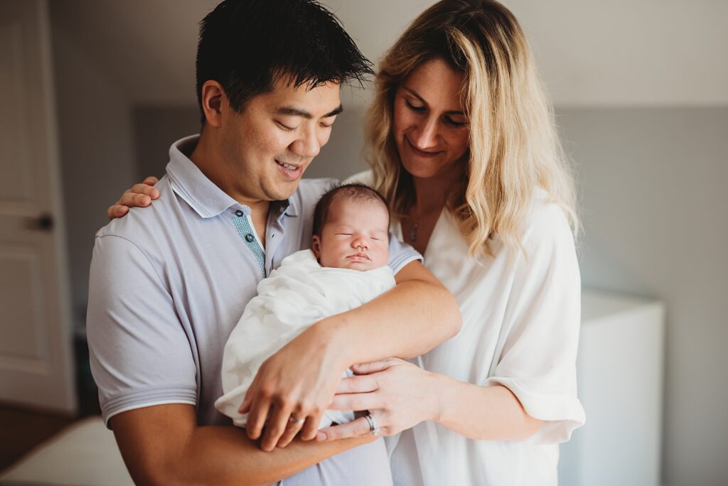 New parents holding their sleeping newborn baby together during a natural lifestyle newborn photography session in Hollis NH