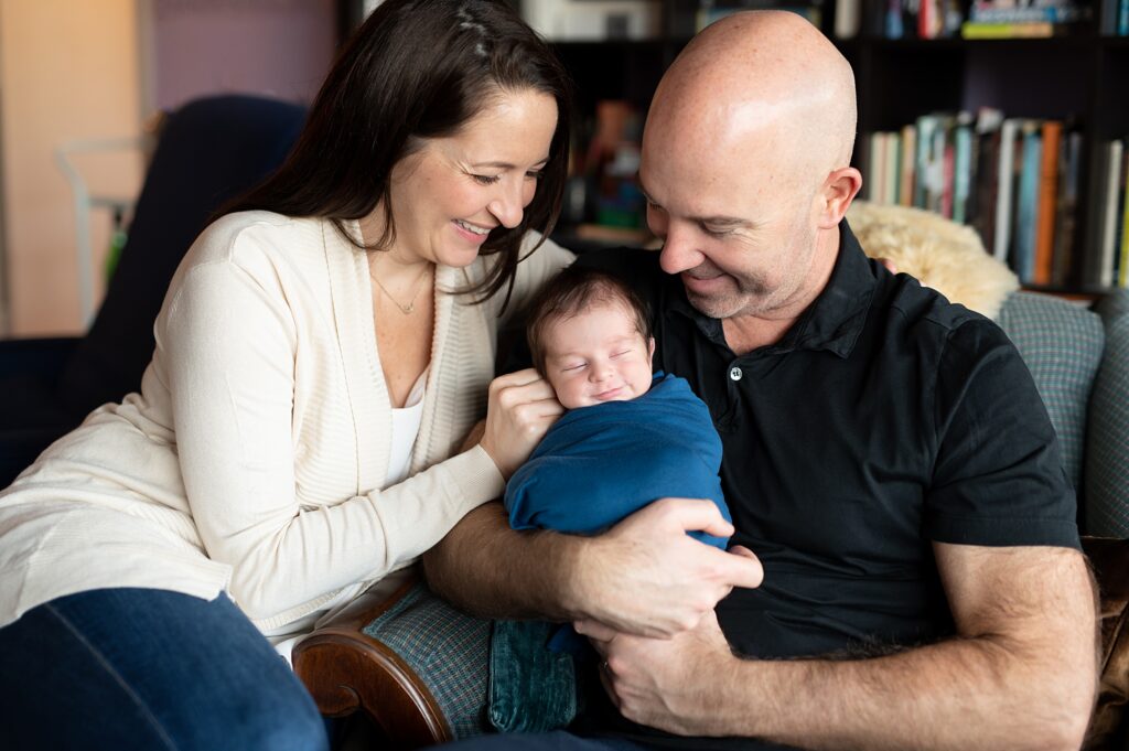 Parents and newborn baby relaxing together on the couch during a lifestyle newborn session in Boston Ma