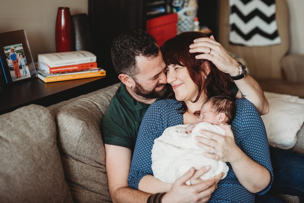 Parents and newborn baby cuddling together on the couch during a lifestyle newborn session in Boston