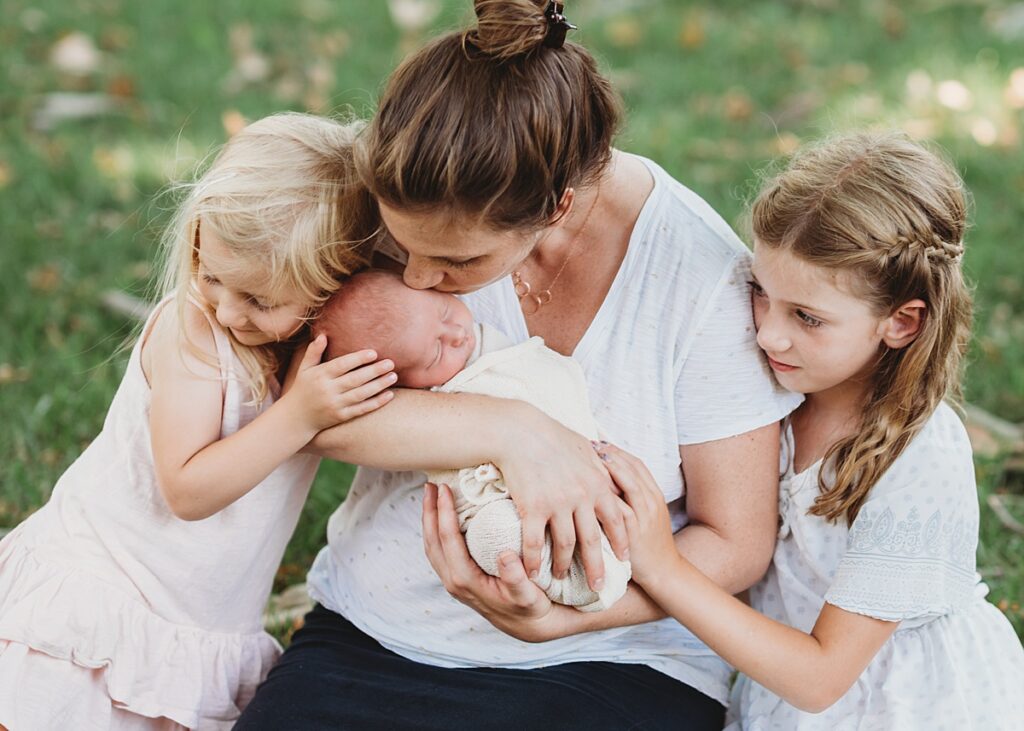 Mother with daughters holding newborn during outdoor lifestyle newborn photography session in Groton MA