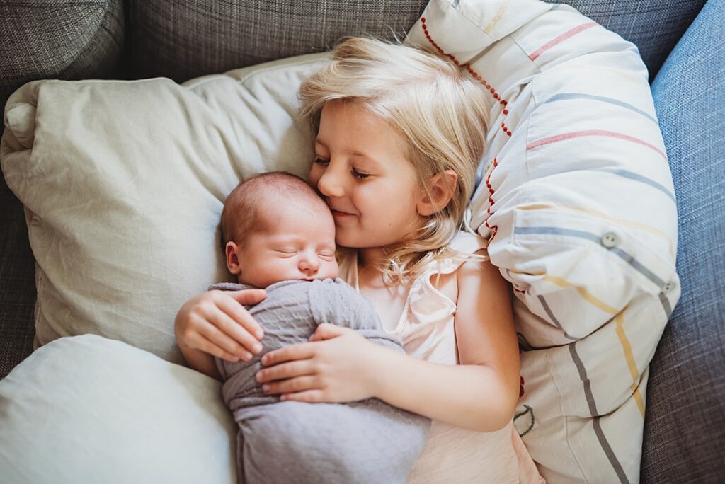Toddler kissing newborn baby during in-home newborn photography session